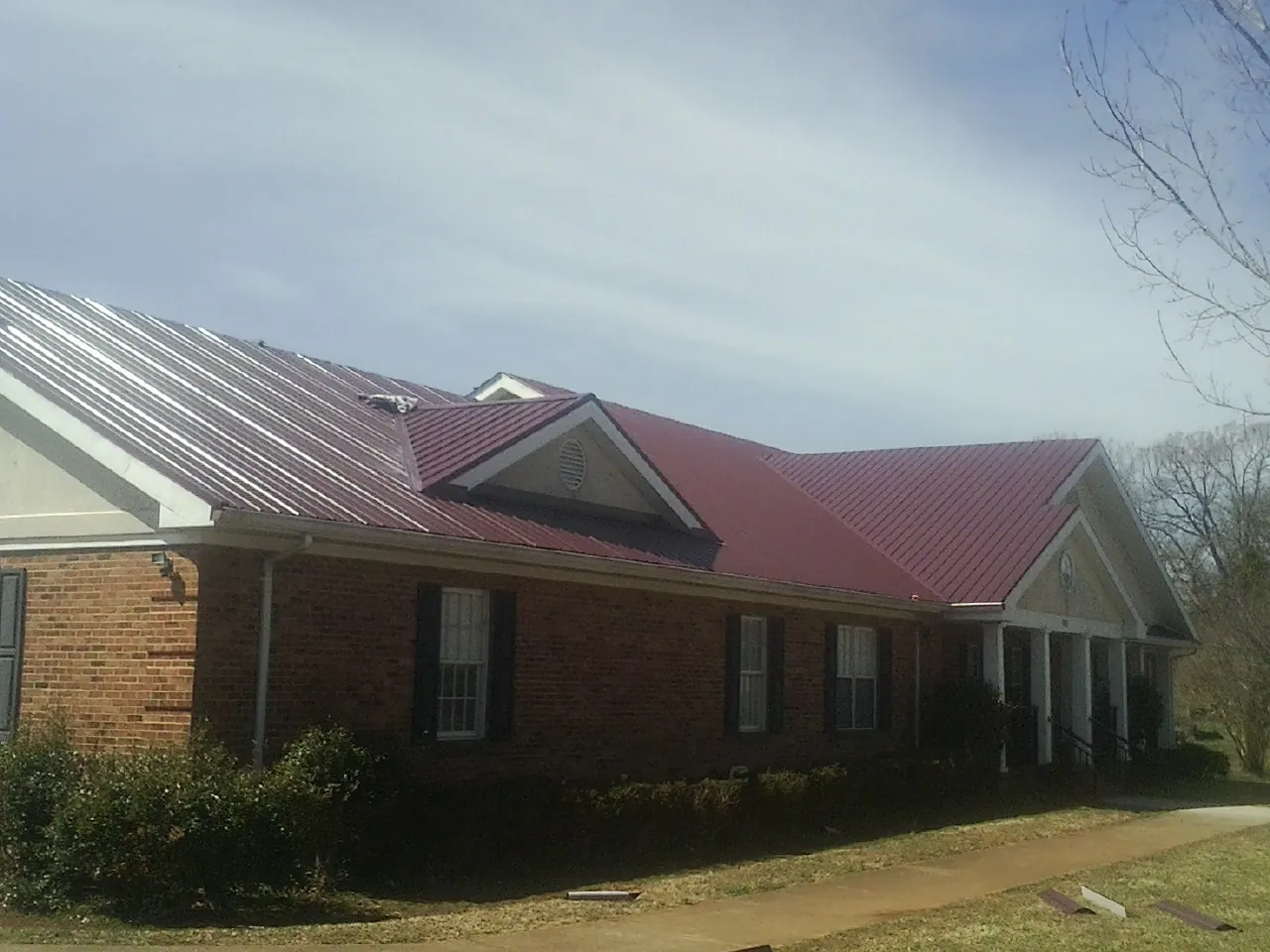 Red metal roof with gabled entries on a long brick building, from a Hail Damage Roof Repair job in Boones Mill
