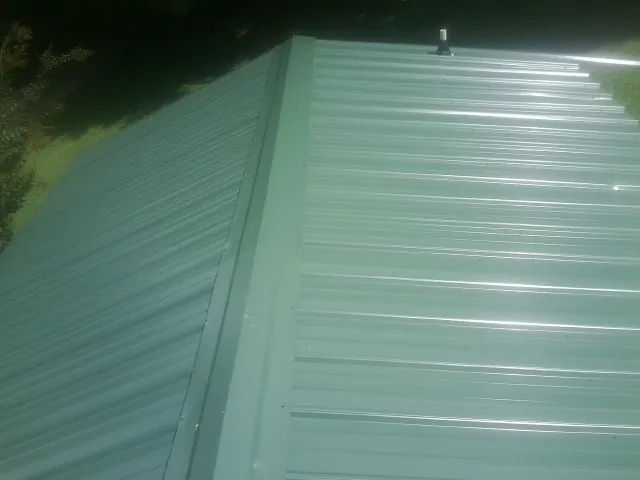 New green metal panels meeting at the ridge of a roof — Flat Roof Repair work by our crew in Boones Mill
