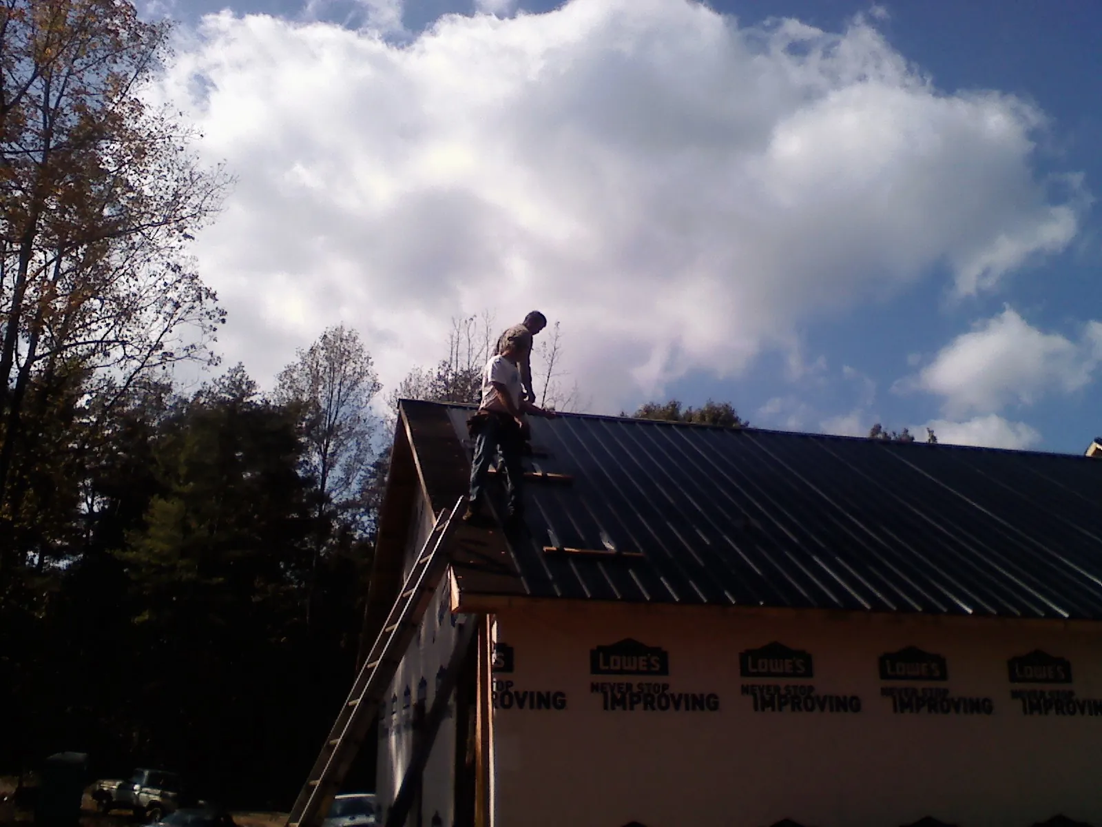 Roofer fastening dark metal panels high against a cloudy sky, from a Roof Inspection job in Boones Mill