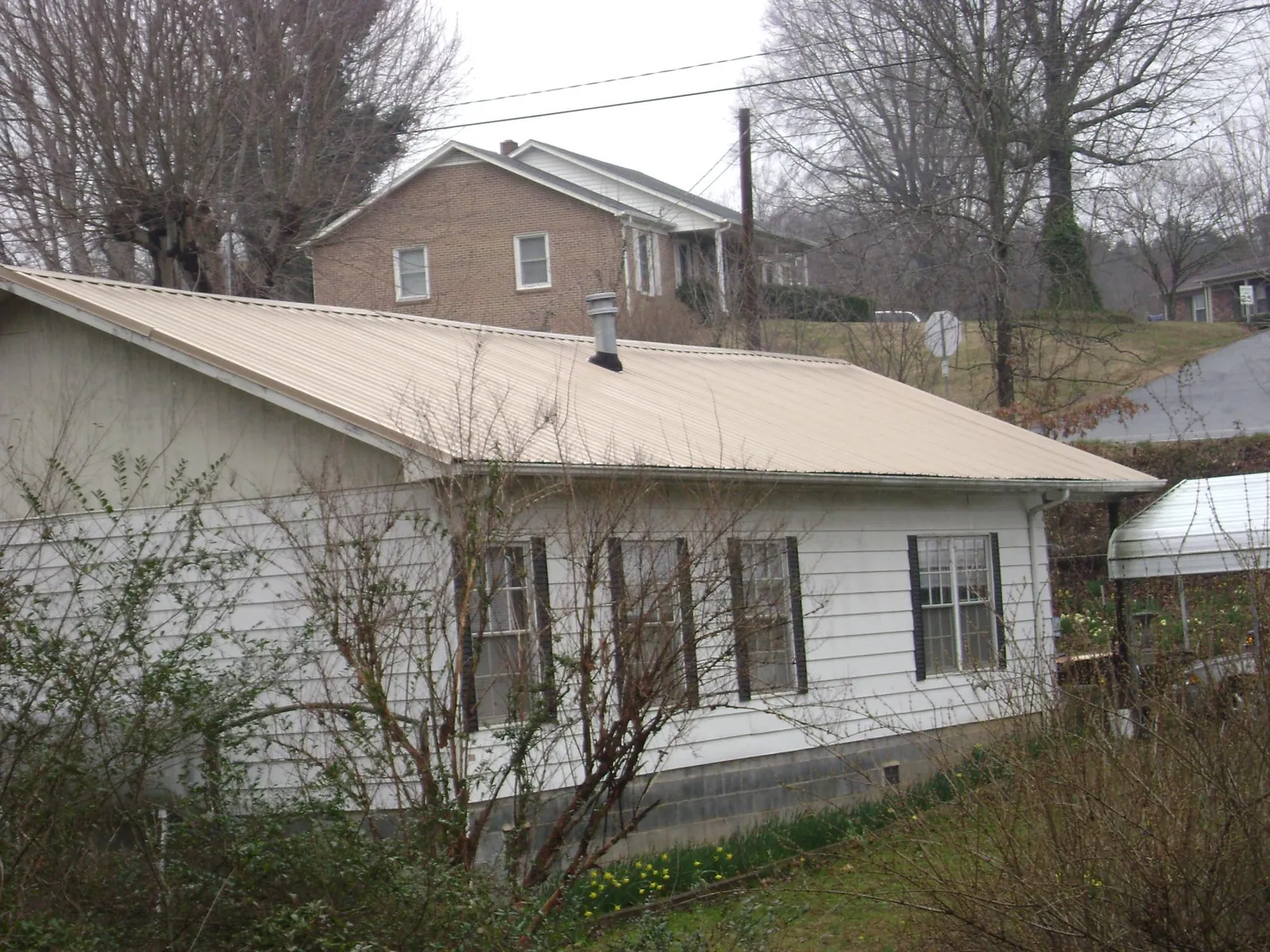 Tan metal roof on a white sided house set into a hillside — Commercial Roofing by Roofing Brothers in Boones Mill